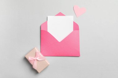 İçinde boş kart, kağıt kalp ve gri arka planda hediye kutusu olan bir zarf. Sevgililer Günü kutlaması