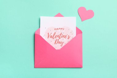 Zarfın içinde hediye kartı ve turkuaz arka planda kağıt kalp var. Sevgililer Günü kutlaması