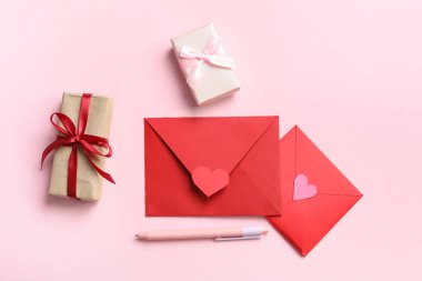 Hediye kutuları ve pembe arka planda kalemleri olan zarflar. Sevgililer Günü kutlaması