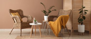 Rahat hasır koltukları, katlanabilir ekranı ve kahverengi duvarın yanındaki masaları olan modern odanın içi.