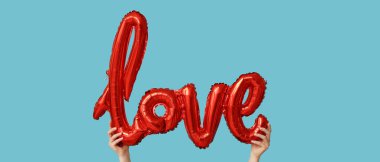 Açık mavi arka planda aşk sözcük şeklinde balon tutan eller. Sevgililer Günü kutlaması