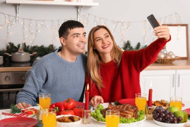 Genç çift Noel arifesinde mutfaktaki masada selfie çekiyor.