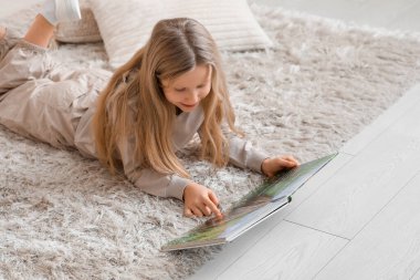 Evde yerde uzanmış kitap okuyan küçük bir kız.