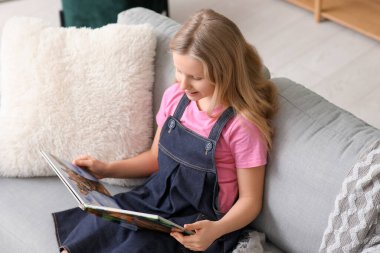 küçük bir kız evde kanepede otururken kitap okuma