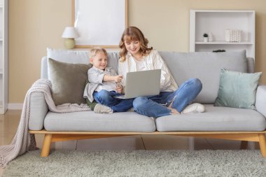 Mutlu anne ve dizüstü bilgisayarı olan küçük oğlu evdeki oturma odasında oturuyor.