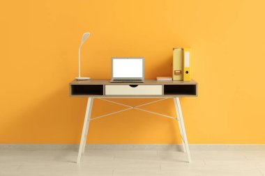 Ofiste sarı duvarın yanında dizüstü bilgisayarı ve lambası olan işyeri