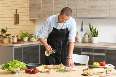 Genç adam mutfaktaki çiğ ete yağ döküyor.