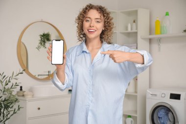 Banyodaki boş cep telefonunu gösteren genç bir kadın.