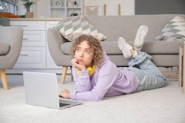Evde dizüstü bilgisayar kullanan üzgün genç bir kadın.