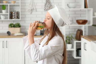 Evdeki mutfakta lezzetli bir burger yiyen tatlı bir aşçı.