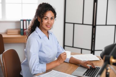 Ofiste dizüstü bilgisayar ve kahve fincanıyla çalışan güzel bir Afro-Amerikan avukat.