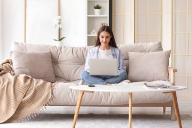 Beautiful young happy woman with laptop sitting on sofa at home