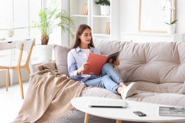 Evdeki kanepede dergi okuyan genç ve güzel bir kadın.