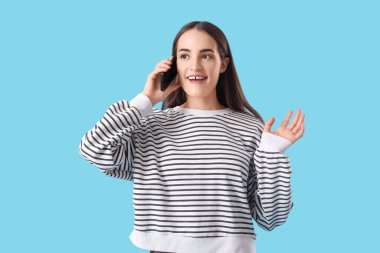 Mavi arka planda cep telefonuyla konuşan güzel, genç bir kadının portresi.