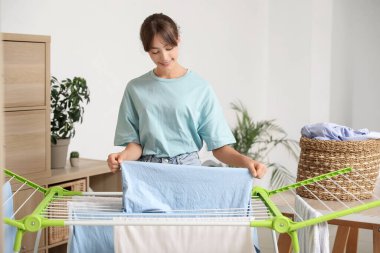 Çamaşır odasında temiz çamaşırları kurutucuya asan genç bir kadın.