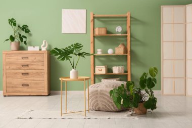 İçinde tropikal canavar yaprakları olan modern oturma odasının masası ve şık bir pouf.