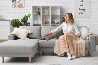 Orta yaşlı bir kadın evdeki kanepede kedi besliyor.