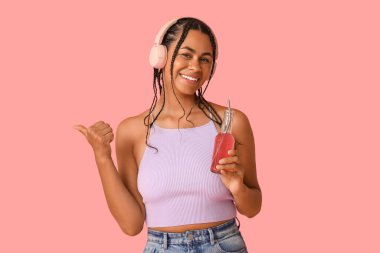 Limonatalı genç Afro-Amerikalı kadın pembe arka planda müzik dinliyor.