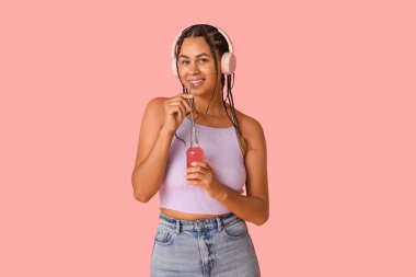 Limonatalı genç Afro-Amerikalı kadın pembe arka planda müzik dinliyor.
