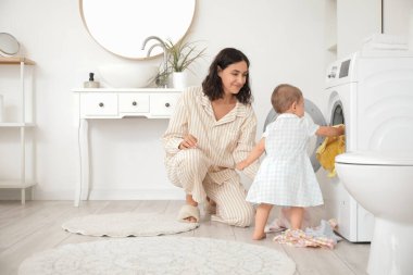 Anne ve küçük bebeği evde çamaşır yıkıyorlar.