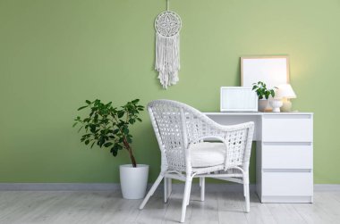 Laptop, ev bitkisi ve yeşil duvarın yanında parlayan masa lambasıyla modern çalışma alanı