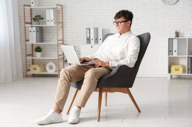 Ofisteki koltukta dizüstü bilgisayarla çalışan yakışıklı bir iş adamı.