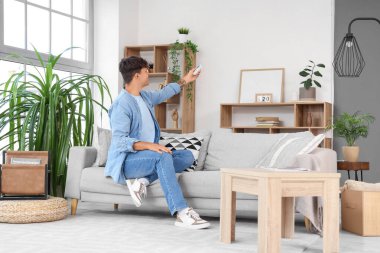 Evdeki kanepede klimayı açan yakışıklı genç adam.