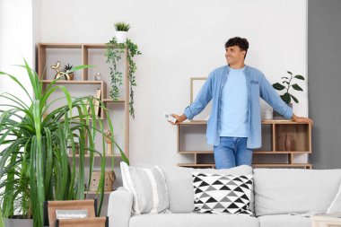 Evinde klima uzaktan kumandası olan mutlu bir genç adam.