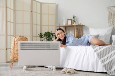 Yatak odasındaki elektrikli ısıtıcının yanında yatan genç kadın.