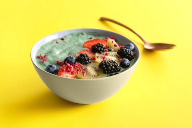 Sarı arka planda lezzetli spirulina smoothie ve meyveli kase, yakın plan.