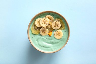 Mavi arka planda lezzetli spirulina smoothie, muz, kivi ve chia tohumları ile kase