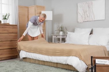 Otel odasında yatağı yapan orta yaşlı oda hizmetçisi.