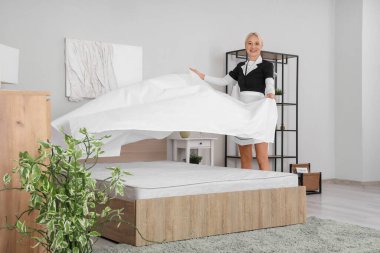 Otel odasında yatağı yapan orta yaşlı oda hizmetçisi.