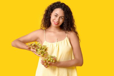 Sarı arka planda olgun üzümleri olan güzel Afro-Amerikalı bir kadın.