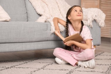 Kitapla evde oturan düşünceli küçük kız.