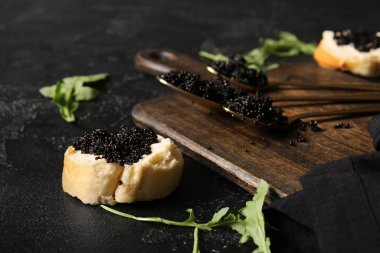 Koyu arkaplanda lezzetli siyah havyarlı kaşık ve baget dilimi.