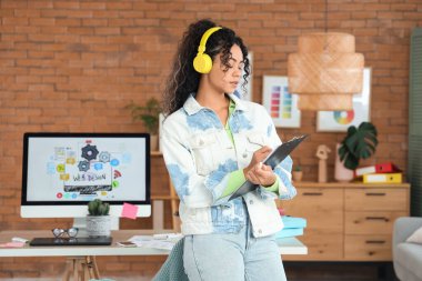 Ofisteki panoya kulaklık takan Afro-Amerikalı kadın web tasarımcısı.