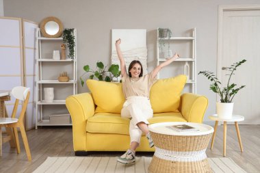 Evdeki sarı kanepede dinlenen genç kadın.