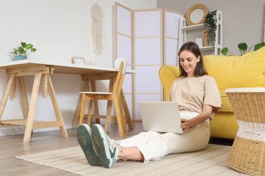 Evde dizüstü bilgisayar kullanan genç bir kadın.