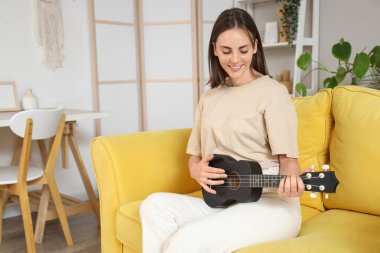 Evdeki kanepede gitar çalan genç bir kadın.