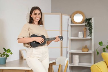 Evde ukulele çalan genç bir kadın.