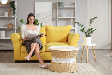 Güzel genç kadın evde kanepenin üzerinde dergi okuma