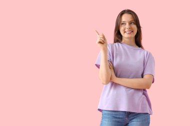 Leylak tişörtlü genç kadın pembe arka plandaki bir şeyi işaret ediyor.