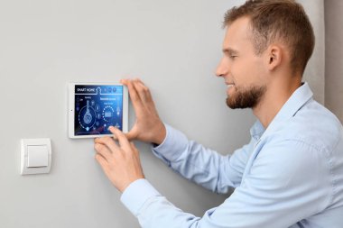 Genç adam ışık duvarında akıllı ev kontrol paneli kullanıyor.