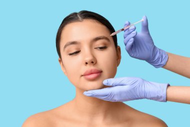 Genç bir kadın mavi arka planda alnına enjeksiyon yaptırıyor.