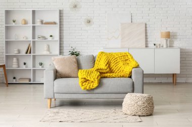 Modern oturma odası, şık gri kanepe, puf ve sarı ekose örgü.