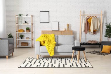 Modern oturma odası, şık gri kanepe, tabure ve sarı ekose örgü.