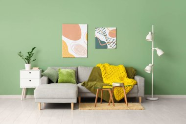 Modern oturma odası, şık bir kanepe, masalar ve sarı örülü ekose kumaş.