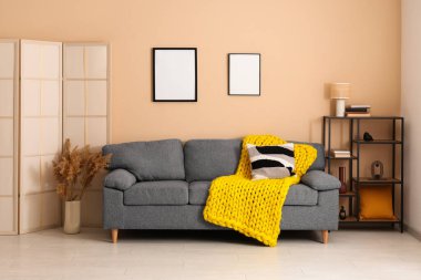 Modern oturma odası, şık gri kanepe, yastık ve sarı ekose örgü.