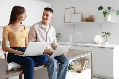 Genç çift mutfakta dizüstü bilgisayar kullanıyor.